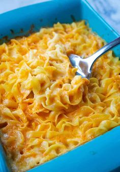 a blue casserole dish filled with macaroni and cheese, topped with a spoon