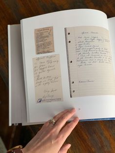 an open book with writing on it and someone's hand next to the page