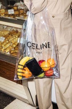 a person holding a plastic bag full of food in front of a display case filled with pastries