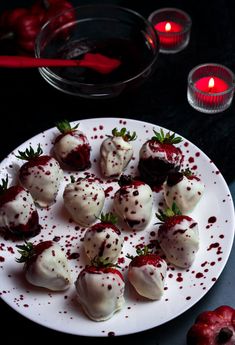 a white plate topped with chocolate covered strawberries next to a red candle and bowl of cherries