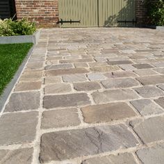 a brick driveway with grass and bushes in the background