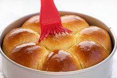 a red brush is sticking into a baked buns in a pan on the table