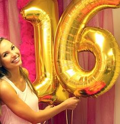 a woman holding a large gold number sixty balloon