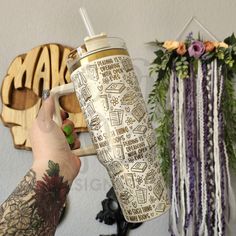 a person holding a coffee cup in front of a wall with flowers and other decorations