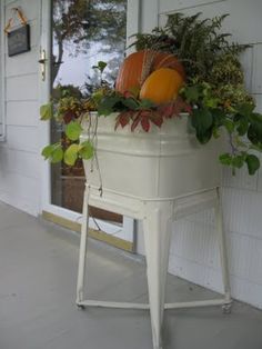 a white planter filled with pumpkins and greenery on the front door porch