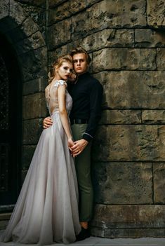 a man and woman standing next to each other in front of a stone wall