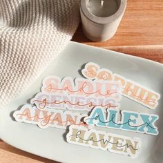 some type of stickers on a plate next to a cup and napkins with a candle