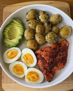 a white plate topped with eggs, meat and potatoes next to an avocado