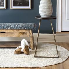 a white vase sitting on top of a wooden table next to a footstool