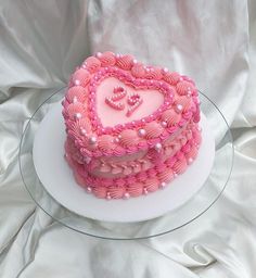 a pink heart shaped cake sitting on top of a white plate with pearls around it