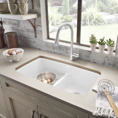 a white kitchen sink sitting under a window next to a counter top with eggs in bowls on it