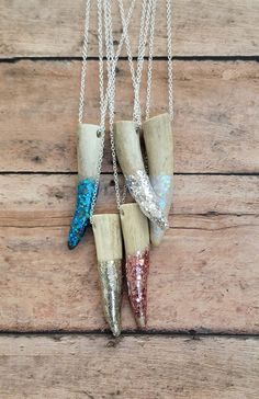 three necklaces that have different colors and designs hanging from chains on a wooden surface