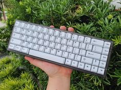 a hand holding a keyboard in front of some bushes and trees with the keys missing