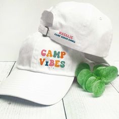 the camp vibes hat is next to a green plant on a white tablecloth