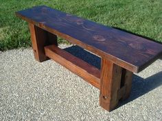 a wooden bench sitting on top of a gravel road next to grass and trees in the background