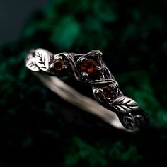 a silver ring with two leaves on it and brown stones in the middle, surrounded by green moss