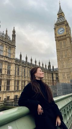 a woman is sitting on a bridge in front of the big ben clock tower