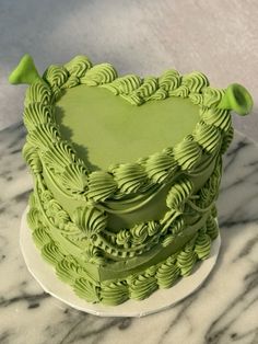 a green heart shaped cake sitting on top of a white plate with marble countertop