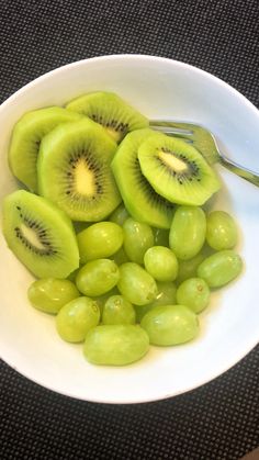 grapes and kiwis in a white bowl with a green spoon on the side