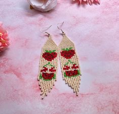 a pair of beaded earrings with roses on them sitting next to some pink flowers