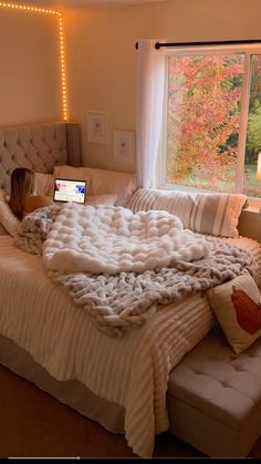 a woman laying on top of a bed under a blanket next to a laptop computer