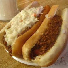 two chili dogs with sour cream on them and a glass of milk in the background