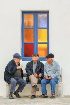 three older men sitting on a bench in front of a building with stained glass windows