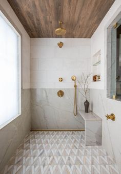 a bathroom with white and gold fixtures, marble flooring and wooden ceiling above the bathtub