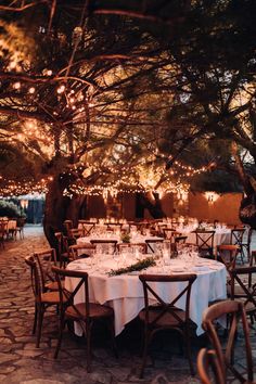 an outdoor dining area with tables and chairs set up for dinner under the shade of a tree