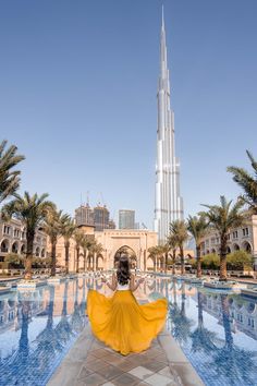 a woman in a yellow dress is looking at the burj tower and pool