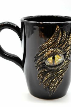 a black coffee mug with an eye and gold feathers on the inside, in front of a white background