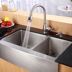 a stainless steel kitchen sink with two faucets and bowls of fruit on the counter