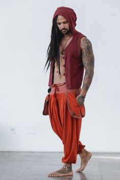 a man with long hair and tattoos wearing an orange outfit standing in front of a white wall