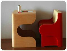 a red chair sitting next to a wooden table with a cup on top of it