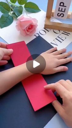 two hands are making a cross out of red and blue paper with pink flowers in the background