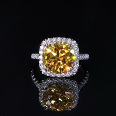 a fancy yellow diamond ring with diamonds around it on a reflective surface in front of a black background