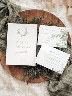 the wedding stationery is laid out on a wooden plate with greenery around it