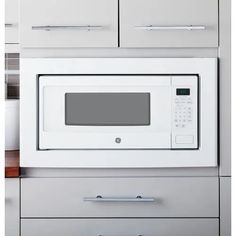 a white microwave oven sitting on top of a kitchen counter next to drawers and cupboards