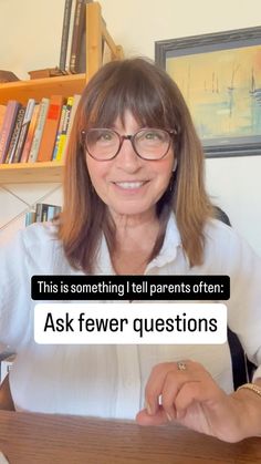 a woman with glasses sitting at a desk in front of a book shelf and holding a piece of paper