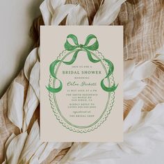 a green and white bridal shower card on top of some feathers with a bow