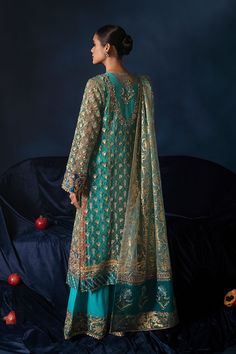 a woman standing in front of an apple tree wearing a green and gold suit with matching dupatta