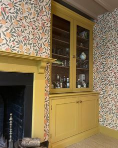 a living room with yellow furniture and floral wallpaper on the walls next to a fire place