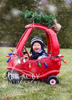 a baby is sitting in a red car decorated with christmas lights and a pine tree