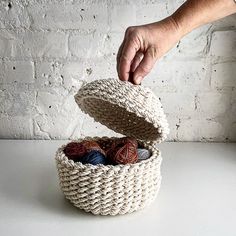 a hand is picking up yarn from a basket on a white table next to a brick wall