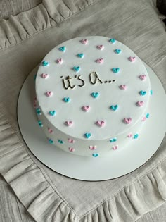 a white cake with pink and blue hearts on it that says it's a