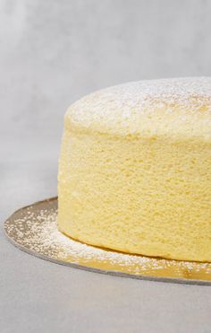 a yellow cake with powdered sugar on top sits on a silver serving platter