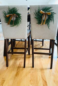 two christmas wreaths on the back of chairs in a room with wood flooring