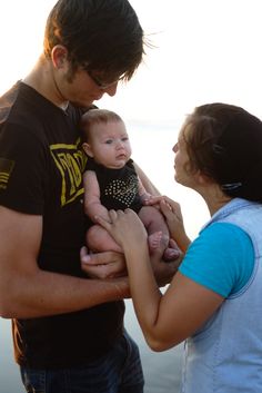 a man holding a baby in his arms while standing next to two other people on the beach