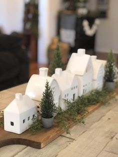 a wooden table topped with small white houses and potted trees on top of it