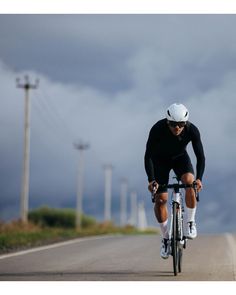 a man riding a bike down the middle of a road under a cloudy blue sky